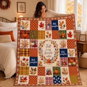 May include: A patchwork quilt featuring a central cream-colored square with the text "Fall is my favorite color" surrounded by a wreath of autumn leaves. The quilt includes squares with pumpkins, maple leaves, plaid patterns, and polka dots.