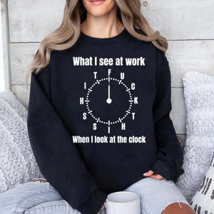 May include: Black sweatshirt with white text: "What I see at work" above a clock graphic with the letters T, F, U, C, K, T, H, S, I, H, S. Below the clock graphic is the text: "When I look at the clock."