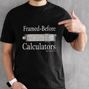 May include: Black t-shirt with the text "Framed-Before Calculators" and a slide rule graphic. The shirt also includes the text "Est. Feb 1970". The shirt is a classic crew neck style.