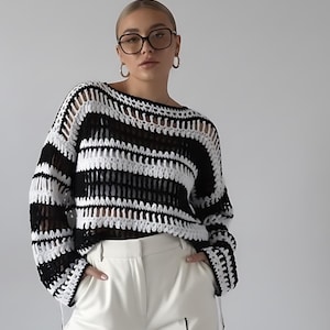 May include: A black and white striped crochet sweater with long sleeves. The sweater has a loose, open weave design. The model is wearing white trousers. The sweater is a stylish addition to any wardrobe.