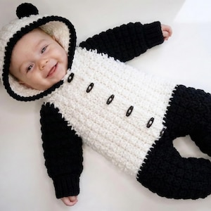 May include: A baby wearing a handmade panda bear outfit. The outfit is white with black accents, including the hood, sleeves, and pants. The hood has black ears. The outfit has black buttons down the front.