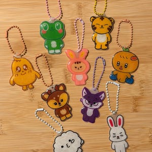 Könnte beinhalten: Eine Sammlung bunter Schlüsselanhänger mit Cartoon-Charakteren. Die Schlüsselanhänger zeigen verschiedene Tiere und Kreaturen, darunter ein Frosch, ein Tiger, ein Hase, ein Reh, ein Fuchs und eine Wolke. Jeder Schlüsselanhänger hat eine Metallkette und einen Ring zur Befestigung.