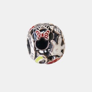 May include: A silver charm with a Minnie Mouse design. The charm features a black Minnie Mouse head with a red bow, a white glove, and other colourful accents. The charm is spherical and has the text "S925" on the side.