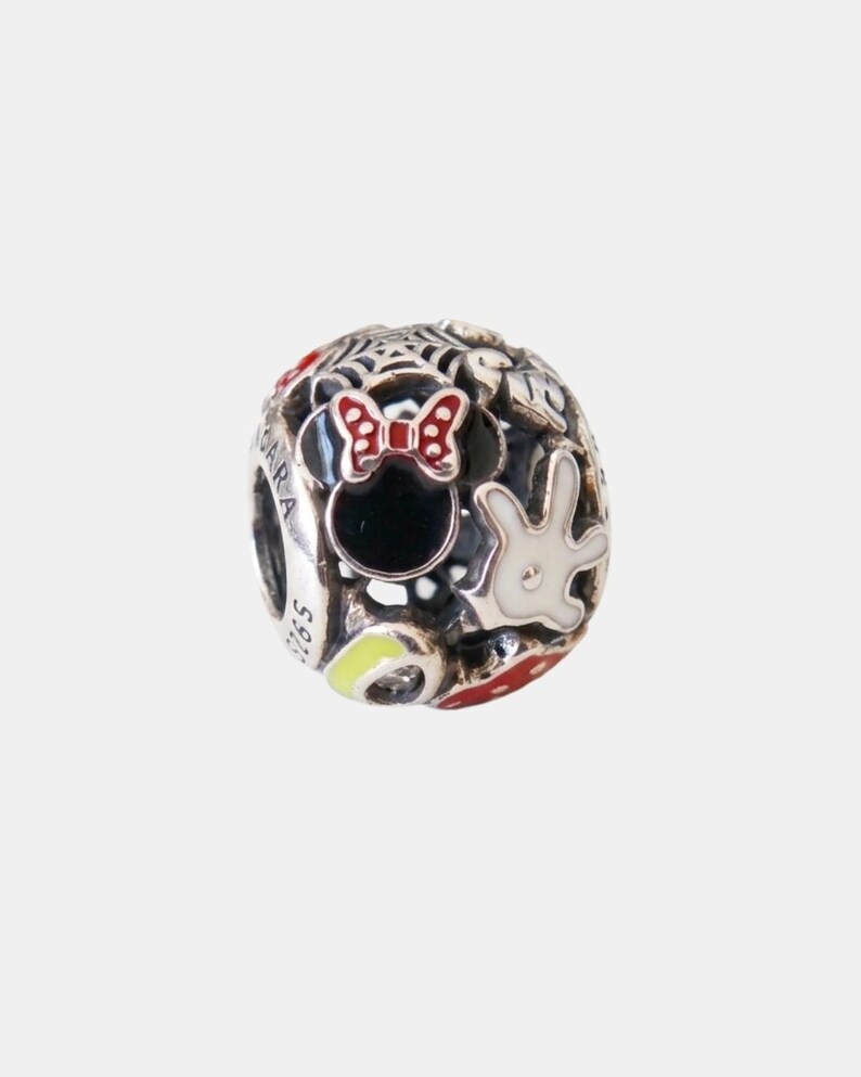 May include: A silver charm with a Minnie Mouse design. The charm features a black Minnie Mouse head with a red bow, a white glove, and other colourful accents. The charm is spherical and has the text "S925" on the side.