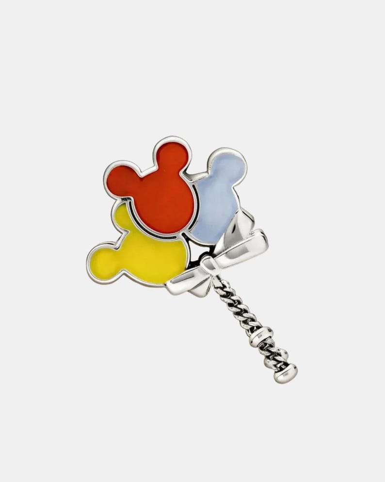 May include: A silver-toned pin featuring three Mickey Mouse head-shaped balloons in red, yellow, and light blue. The balloons are connected to a silver chain and bow.
