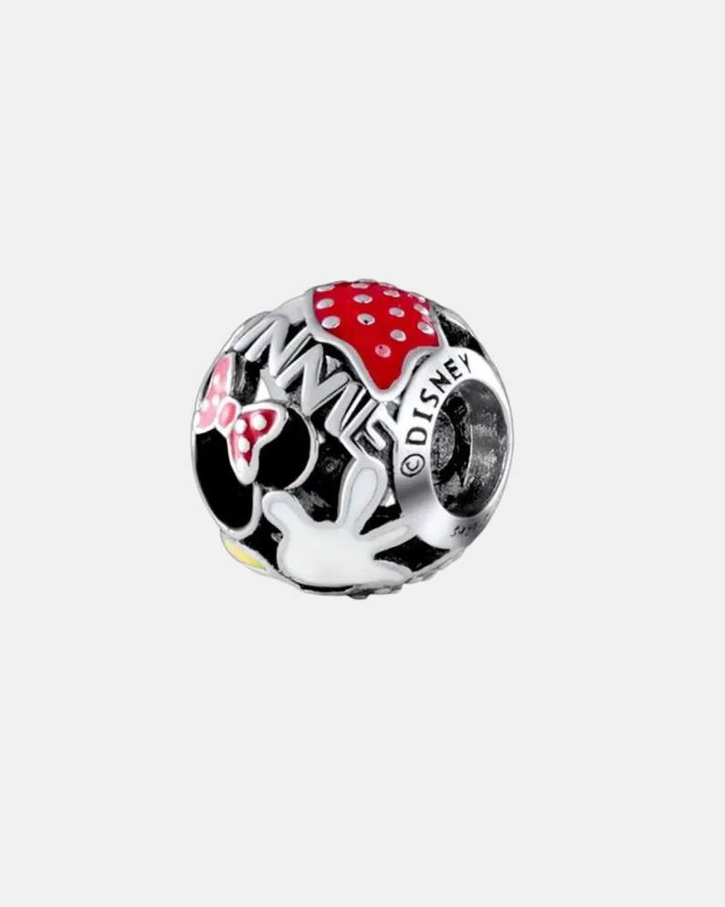 May include: A silver charm with a Minnie Mouse theme. The charm features a red polka-dot bow, the word "MINNIE" in black, a red polka-dot design, and a white glove. The word "DISNEY" is also visible.