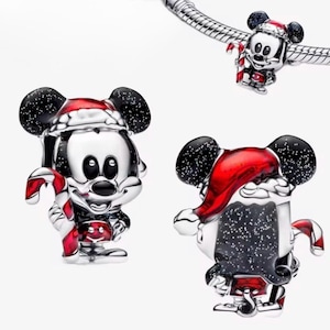 May include: Silver Mickey Mouse charm with black ears and a red Santa hat. The charm is holding a red and white candy cane. One charm is attached to a silver bracelet. Festive holiday jewellery.