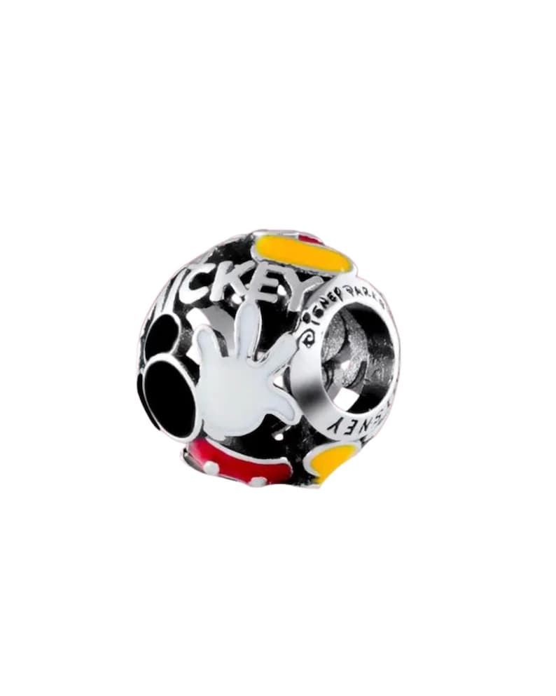Puede incluir: Un charm plateado con fondo negro y la palabra "MICKEY" en blanco. El charm presenta una mano blanca con detalles rojos y amarillos, y tambi&eacute;n se ve la palabra "DISNEY".