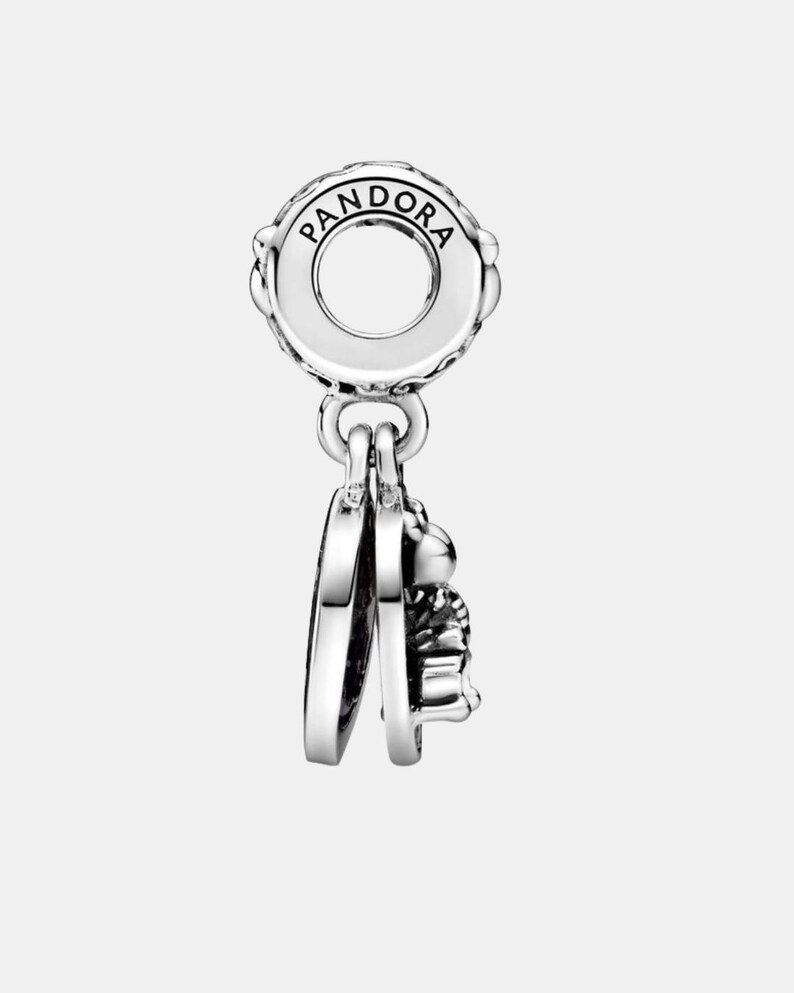 May include: A silver charm with the brand name "PANDORA" engraved on the top. The charm features a circular design with a dangling heart and a small, detailed object, possibly a bee or similar insect.
