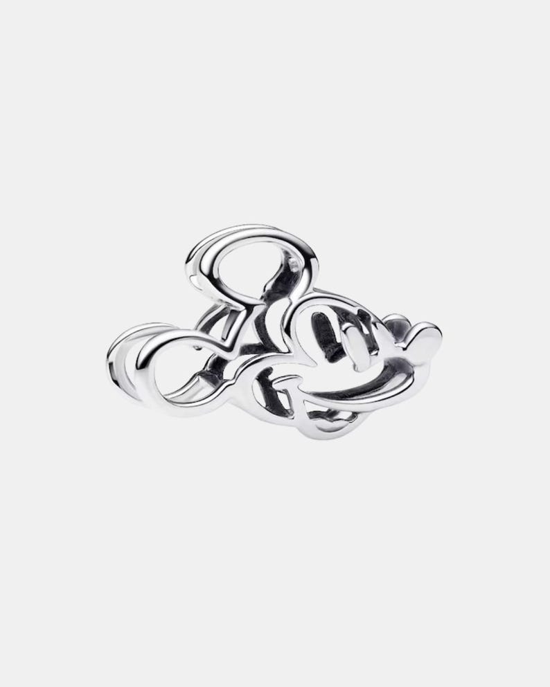 May include: A silver charm in the shape of Mickey Mouse's head. The charm is made of a shiny, reflective metal and features the iconic mouse's silhouette with its large ears and smiling face. The charm is a collectible item.