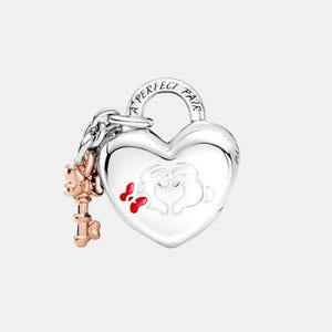 May include: A silver heart-shaped charm with the words "A PERFECT PAIR" engraved on the top. The charm features a design of two hands forming a heart with red accents. A rose gold key charm hangs from a chain attached to the heart.