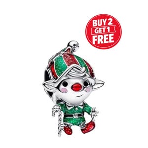 May include: A silver-toned metal charm shaped like an elf wearing a green and red glittery hat and outfit, featuring a red nose, a candy cane accessory, and a small bell on the hat tip. A red circular badge displays the text BUY 2 GET 1 FREE.