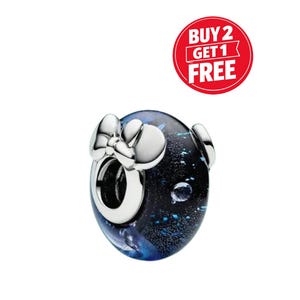 May include: A round charm bead featuring a dark blue and black glass body with shimmering blue flecks and a silver-toned metal bow accent on the front. A red circular graphic in the upper right corner displays the white text BUY 2 GET 1 FREE.