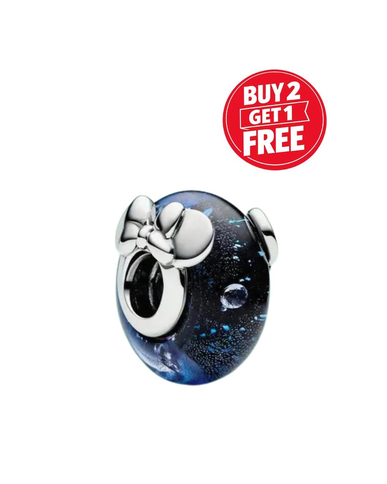 May include: A round charm bead featuring a dark blue and black glass body with shimmering blue flecks and a silver-toned metal bow accent on the front. A red circular graphic in the upper right corner displays the white text BUY 2 GET 1 FREE.