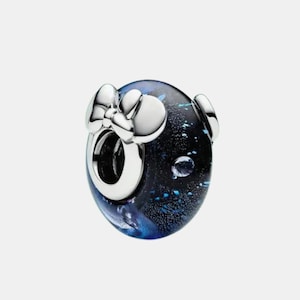 May include: A round charm bead featuring a dark blue and black glass body with shimmering flecks and a silver-toned metal core. The bead is accented with a polished silver-toned metal bow detail attached to the front, surrounding the central opening.
