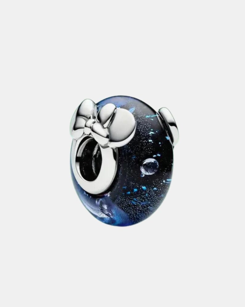 May include: A round charm bead featuring a dark blue and black glass body with shimmering flecks and a silver-toned metal core. The bead is accented with a polished silver-toned metal bow detail attached to the front, surrounding the central opening.