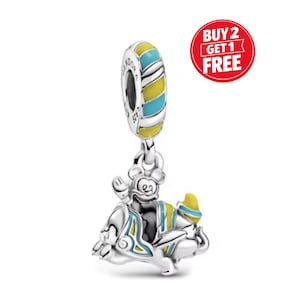 May include: A silver charm with a cartoon character design. The charm features a yellow and blue striped ring at the top, with a character below wearing a yellow and blue outfit. The charm has a "BUY 2 GET 1 FREE" sticker in the background.