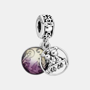 May include: A silver charm with two circular pendants. One pendant features a purple and white landscape scene. The other pendant has a 3D image of two bears on a swing. The charm has a heart-shaped design.