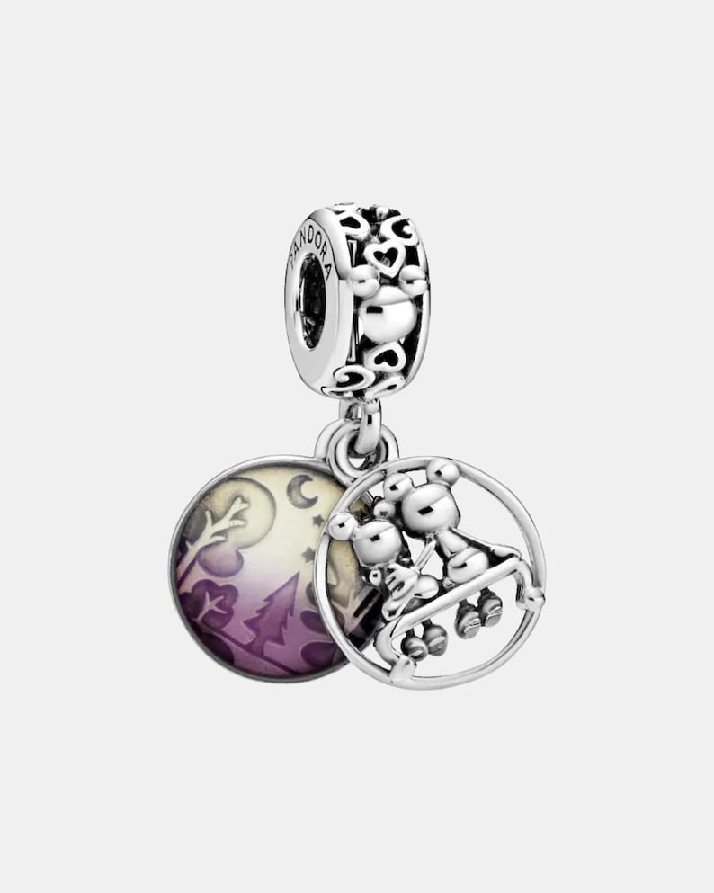 May include: A silver charm with two circular pendants. One pendant features a purple and white landscape scene. The other pendant has a 3D image of two bears on a swing. The charm has a heart-shaped design.