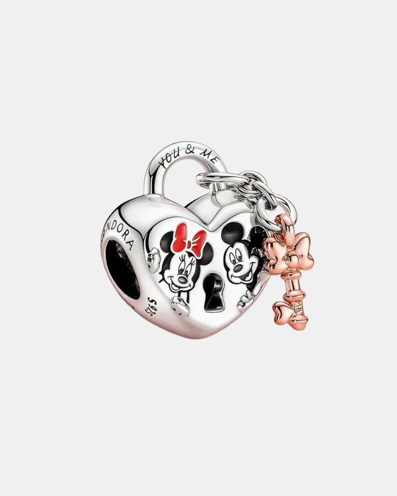 May include: A silver heart-shaped charm featuring Mickey and Minnie Mouse. The charm has a key and bow attached. The words "YOU & ME" are engraved on the top. This is a Disney-themed jewellery item.