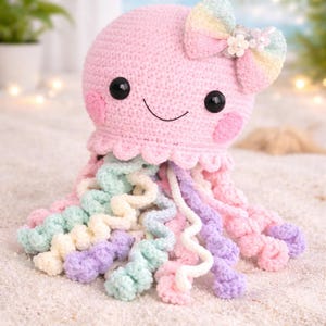 May include: A handmade pink crochet octopus with a smiling face, black eyes, and rosy cheeks. It has a rainbow bow and pastel-colored tentacles. The octopus is a soft toy, perfect for a child's room or as a decorative item.