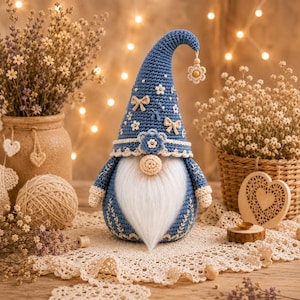 Peut inclure: Une figurine de gnome crochetée en bleu avec un grand chapeau pointu orné de petites fleurs blanches et de nœuds, un nez rond beige et une longue barbe en fausse fourrure blanche. Une breloque fleur pend au bout du chapeau.