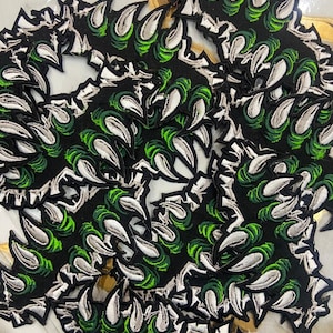May include: A pile of black claw-shaped patches with white and green detailing. The patches have an embroidered design of sharp, curved claws. These patches are likely for decorative use, such as embellishing clothing or accessories.