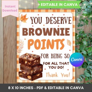Pode incluir: Um cartaz retangular com uma borda xadrez laranja e branca apresentando uma pilha de três brownies de chocolate. O texto diz: YOU DESERVE BROWNIE POINTS FOR BEING SO FOR ALL THAT YOU DO! Thank You! O design inclui ilustrações de folhas de outono.