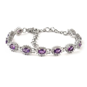 Peut inclure: Un bracelet argenté orné de pierres précieuses ovales violettes entourées de petites pierres claires. Le bracelet présente un design de chaîne délicat et un fermoir sécurisé. Les pierres sont serties dans un motif floral.