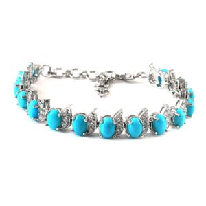 Könnte beinhalten: Ein silberfarbenes Armband mit einer Reihe ovaler, leuchtend türkisfarbener Steine. Jeder Stein ist von kleinen, klaren, funkelnden Akzentsteinen in einer Metallfassung umgeben. Das Armband verfügt über einen feinen Kettengliederverschluss.