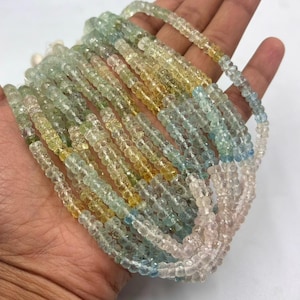 May include: A collection of beaded necklaces in shades of yellow, green, blue, and pink. The beads are small and round, strung together to create multiple strands. The necklaces are held in a hand against a white background.
