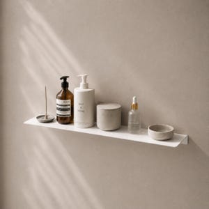 May include: A white wall-mounted shelf holding a small incense holder, a dark amber bottle with a black pump, a white cylindrical bottle labeled Salt & Stone, a matte gray lidded container, a clear glass dropper bottle, and a small gray bowl.
