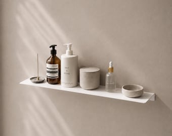 May include: A white wall-mounted shelf holding a small incense holder, a dark amber bottle with a black pump, a white cylindrical bottle labeled Salt & Stone, a matte gray lidded container, a clear glass dropper bottle, and a small gray bowl.