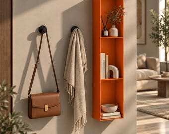 May include: A tall orange wall-mounted shelf with three compartments, holding books, a bowl, and a vase. Beside it, a brown leather shoulder bag and a beige fringed throw blanket hang from two black circular wall hooks.