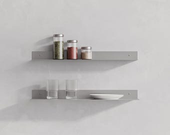 May include: Two horizontal light gray metal wall shelves mounted one above the other. The top shelf holds three glass jars with silver lids containing green herbs, red spices, and brown powder. The bottom shelf holds two ribbed glass tumblers and a white plate.