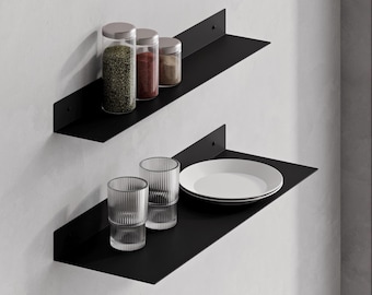 May include: Two matte black metal wall-mounted shelves. The top shelf holds three clear glass spice jars with silver lids. The bottom shelf holds two clear ribbed glass tumblers and a stack of two white ceramic plates, all arranged for storage.
