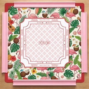 Könnte beinhalten: Eine quadratische Mahjong-Matte mit tropischem Muster aus rosa Flamingos, grünen Palmenblättern, Hibiskusblüten, Kokosnüssen und Ukulelen. Der weiße Mittelbereich zeigt die Buchstaben RWH und Spielanleitungen, eingerahmt von vier rosa Kunststoffschienen.