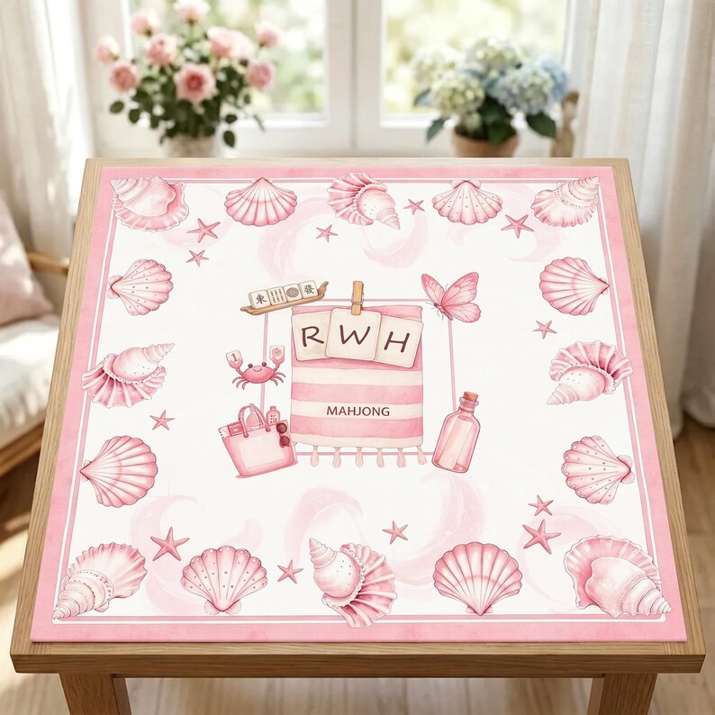 May include: A square pink and white table mat featuring a border of seashells and starfish. The centre displays a beach towel with the letters RWH, a tote bag, a bottle, a crab, a butterfly, and a mahjong tile set with the text MAHJONG.