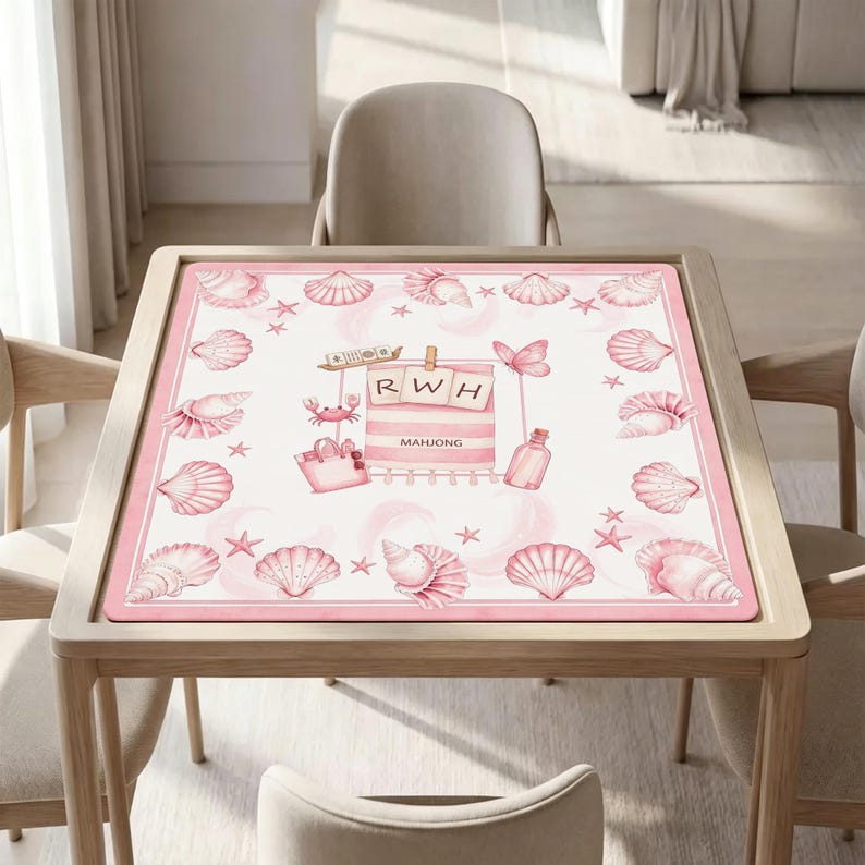 May include: A square mahjong mat featuring a pink and white beach theme with illustrations of seashells, starfish, a crab, a tote bag, and a bottle. The centre displays a pink striped towel with the letters RWH and the word MAHJONG printed.