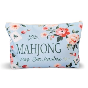 May include: A light blue zippered pouch featuring a floral pattern with pink and peach flowers, green leaves, and mahjong tiles. The text MAHJONG is printed in large dark green letters, accompanied by cursive script text above and below the word.