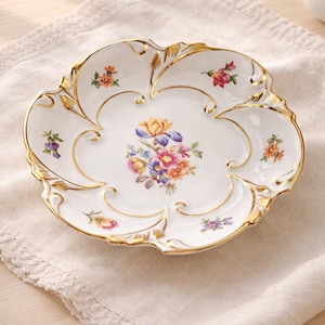 Puede incluir: Plato de porcelana blanca para servir con borde festoneado y ribete dorado. El plato presenta un ramo floral central y pequeños detalles florales. Una pieza decorativa para servir o exhibir.