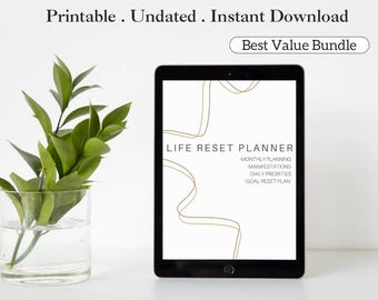 May include: A digital tablet displaying a "Life Reset Planner" with gold accents. The screen shows sections for monthly planning, manifestations, daily priorities, and goal reset. Text above reads "Printable. Undated. Instant Download." A glass vase with green leaves is on the left.