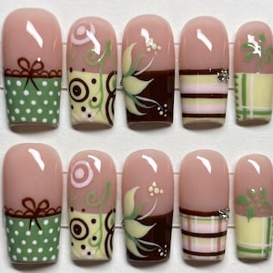 May include: A set of ten press-on nails featuring a nude base with varied designs including green polka dots with brown bows, brown and cream swirls, dark brown floral accents, horizontal brown and pink stripes, and green plaid patterns.