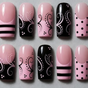 Könnte beinhalten: Ein Set aus zehn künstlichen Nägeln in verschiedenen Designs. Die Nägel weisen eine Kombination aus rosa und schwarzen Farben mit Mustern wie Streifen, Tupfen und wirbelnden floralen Designs auf. Die Nägel sind quadratisch geformt und haben ein glänzendes Finish.