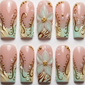 May include: A set of ten press-on nails featuring a nude base with mint green tips. The design includes raised 3D mint green flowers with gold centers, gold swirling line accents, and small white pearl beads arranged across the nail surfaces.