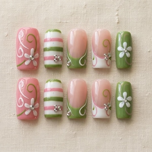 K&ouml;nnte beinhalten: Ein Set aus zehn k&uuml;nstlichen N&auml;geln in verschiedenen Designs. Die N&auml;gel zeigen rosa, gr&uuml;ne und wei&szlig;e Farben mit floralen und gestreiften Mustern. Einige N&auml;gel haben ein French-Tip-Design mit gr&uuml;nen Akzenten und Strasssteinen.