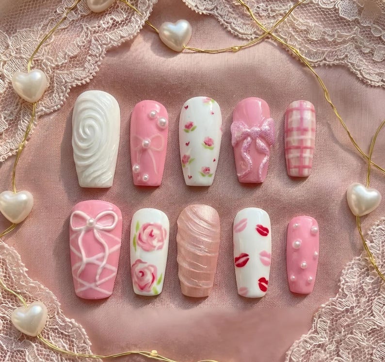 May include: A set of ten artificial nails in various designs. The nails feature a range of pink and white colors, with embellishments like bows, pearls, and floral patterns. Some nails have a textured appearance, while others showcase a plaid design.