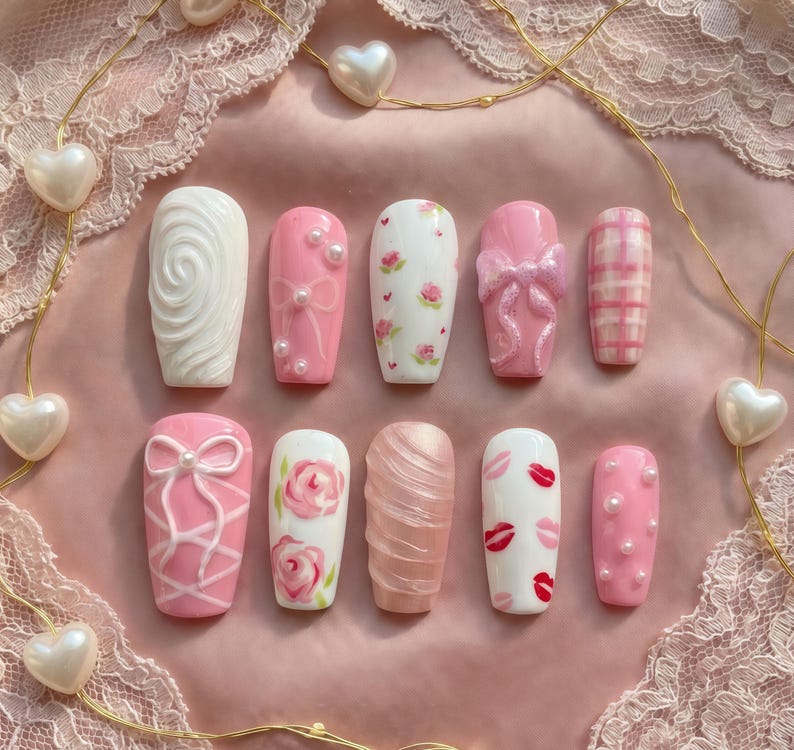 May include: A set of press-on nails in various designs. The nails feature a range of colors, including white and pink, with embellishments like bows, pearls, and floral patterns. Some nails have a textured appearance, while others showcase lip and plaid designs.