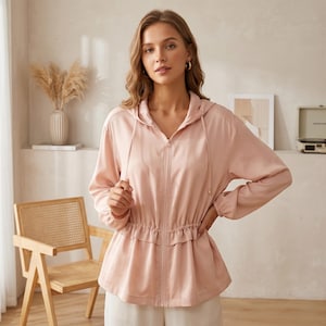 Puede incluir: Chaqueta con capucha rosa claro con cordón y cierre de cremallera. La chaqueta tiene mangas largas y cintura fruncida. La modelo lleva la chaqueta con pantalones blancos. La chaqueta es de material ligero.