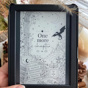 Könnte beinhalten: Ein schwarzer Tolino E-Reader, der eine Fantasy-Illustration mit dem Text "One more chapter" anzeigt. Der Bildschirm zeigt einen Drachen, ein Schloss und gestapelte Bücher mit Titeln wie "Dragonblood" und "Love Power Destiny". Eine Tasse mit einem Mond ist ebenfalls zu sehen.